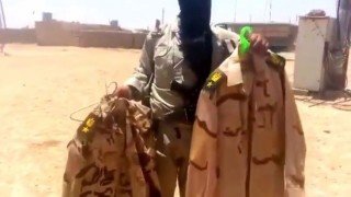 Armed member of ISIL holding up Iraqi soldier uniforms before tossing them on the ground-Mosul, Iraq (June, 11, 2014)